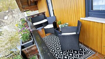 A patio area with wicker furniture, a patterned rug, and potted plants.