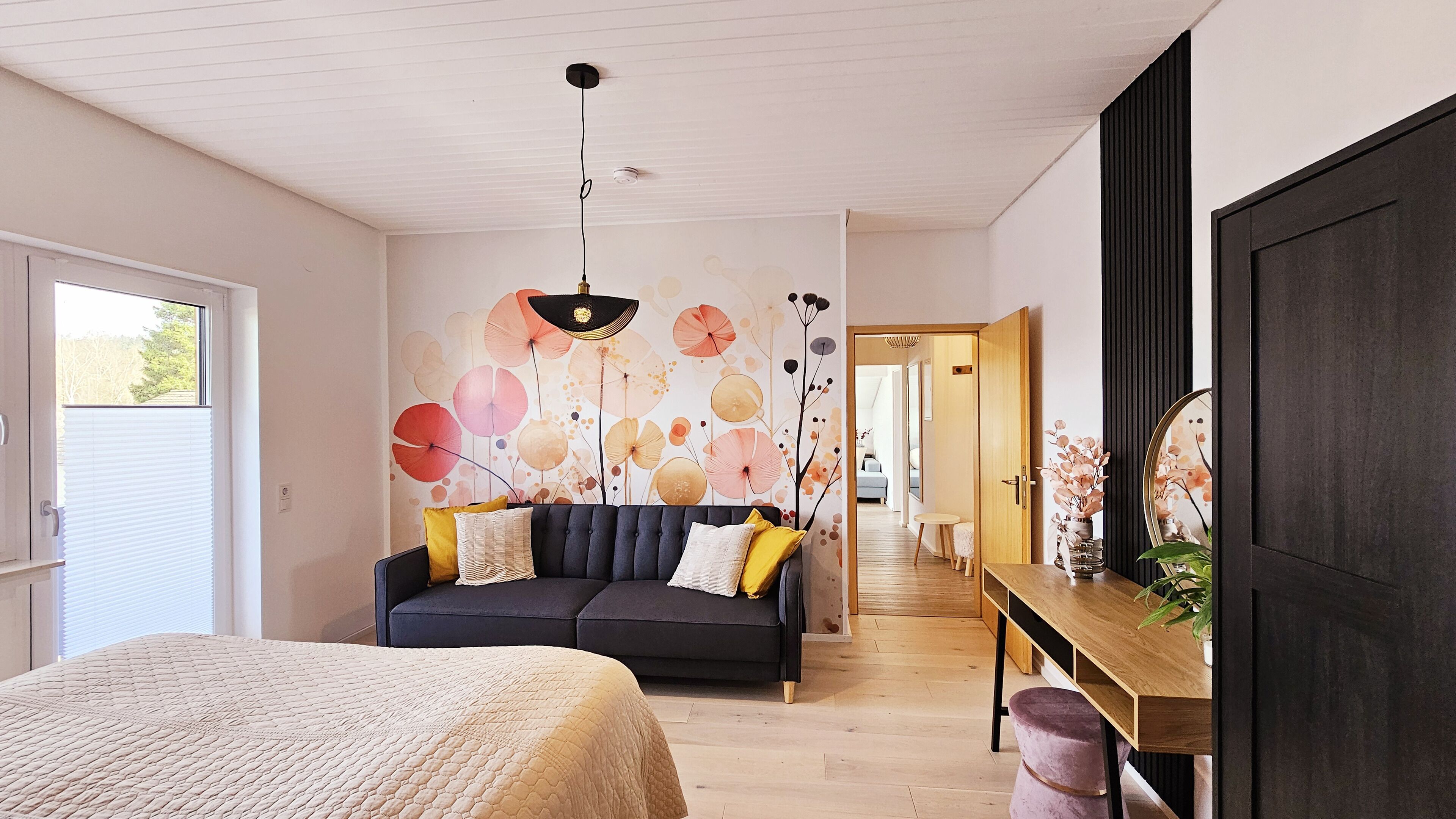 Una camera da letto moderna con un letto, un divano scuro, un tavolo in legno e una parete con motivo floreale.