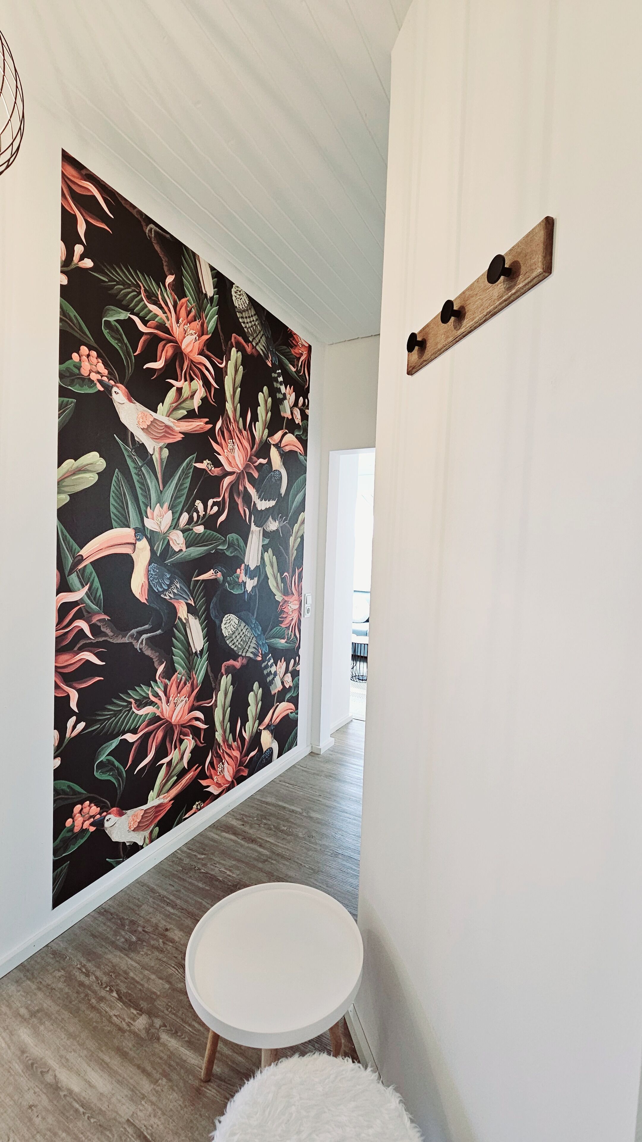 A hallway with a wooden floor, a white round table, and a wall with a tropical floral mural.