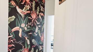 A hallway with a wooden floor, a white round table, and a wall with a tropical floral mural.