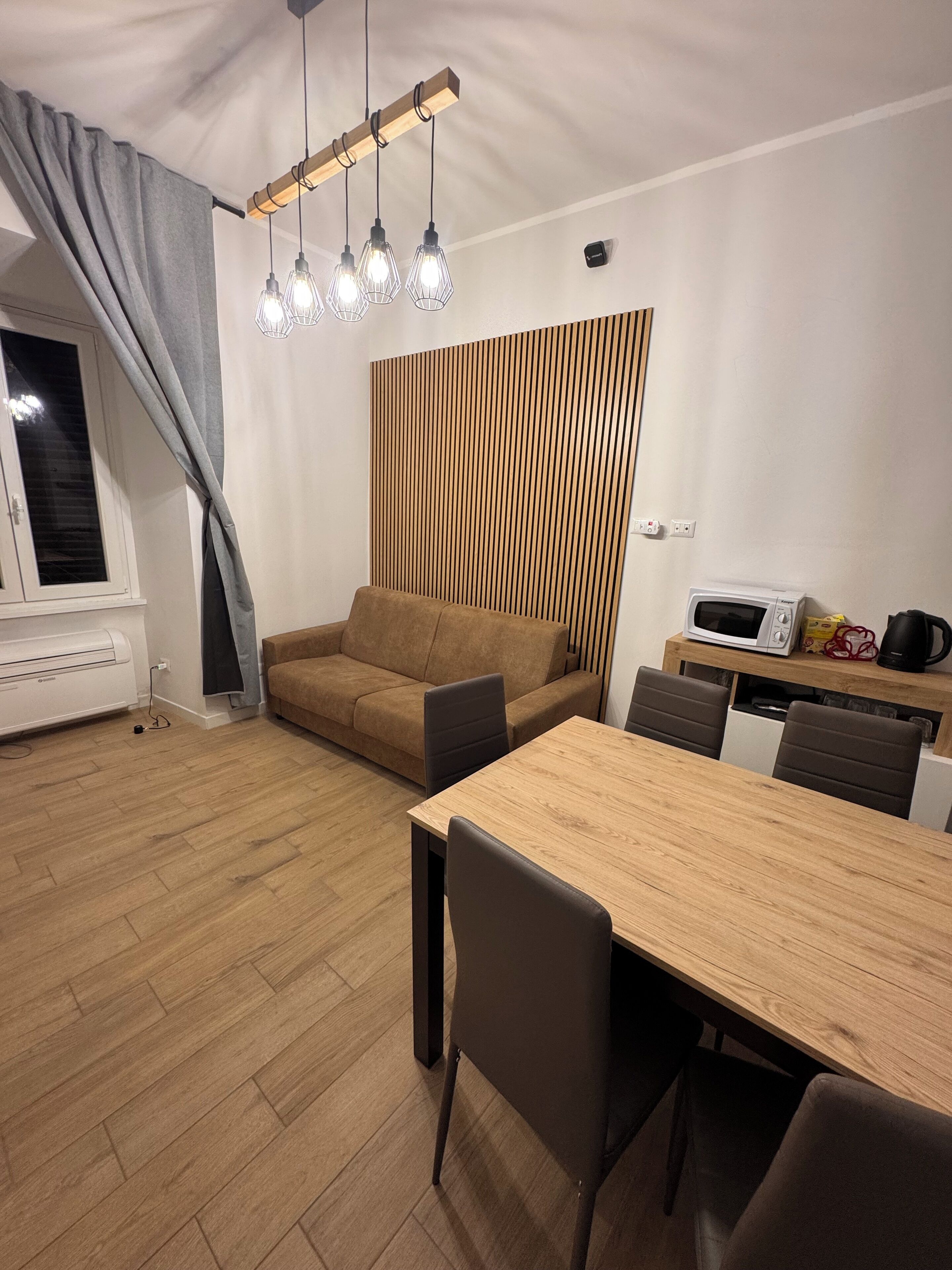 Een moderne woonkamer met een houten eettafel, een bruine bank en een keukenhoek met een magnetron en waterkoker.