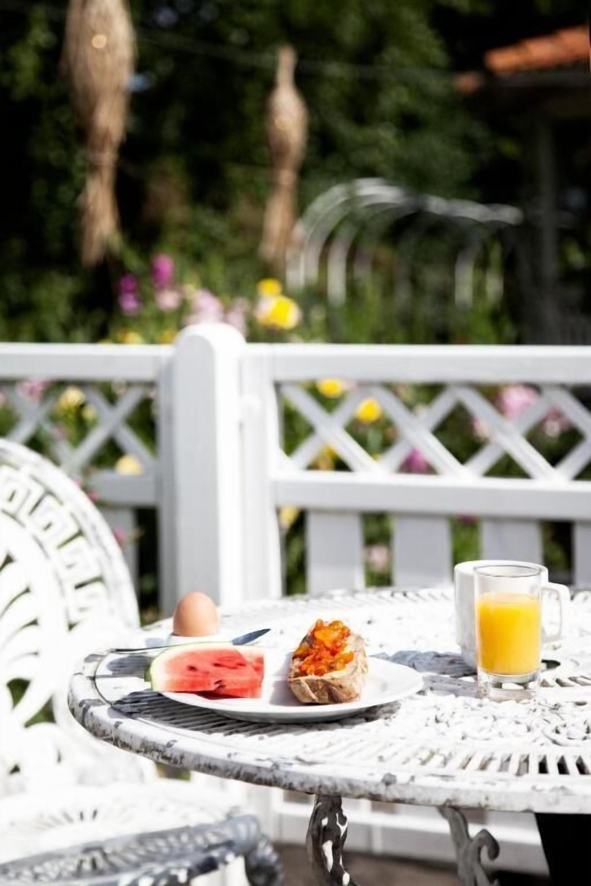 A white metal table with a plate of food, a glass of orange juice, and a white fence in the background.