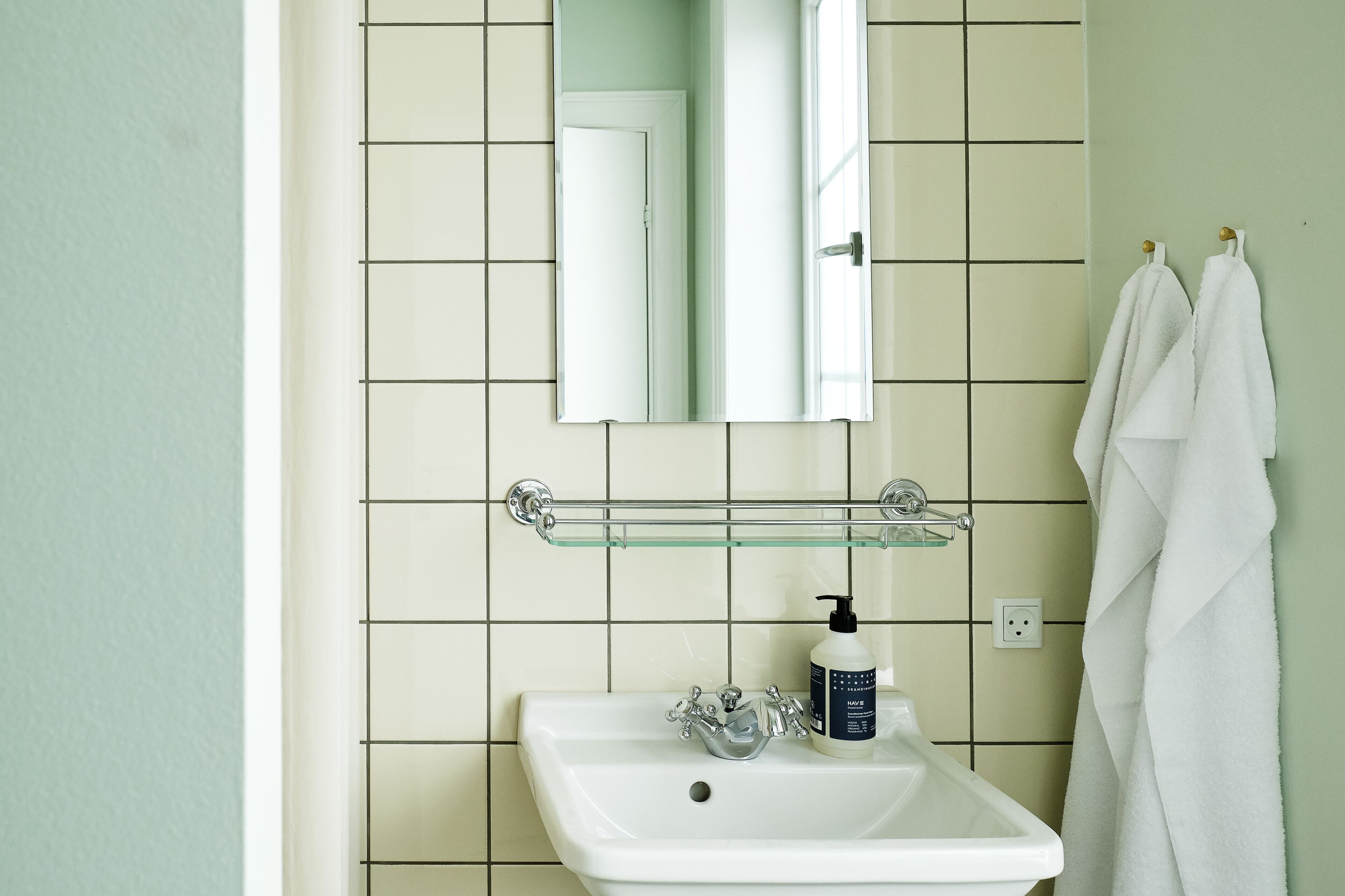 A bathroom with a white sink, a glass shelf above it, a mirror, and a towel rack with two towels.
