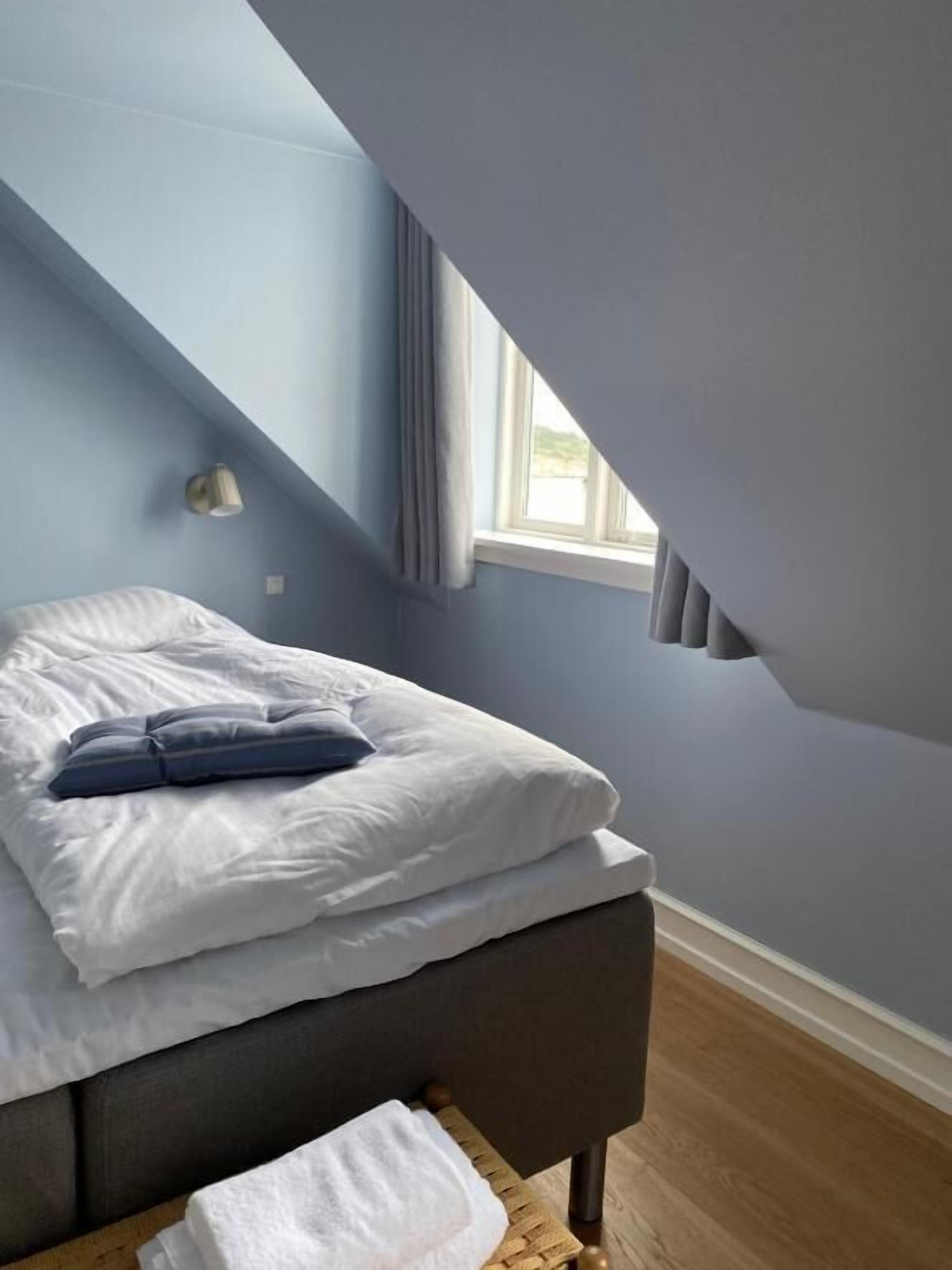 A bedroom with a bed, a bedside table, a window, and a light fixture.