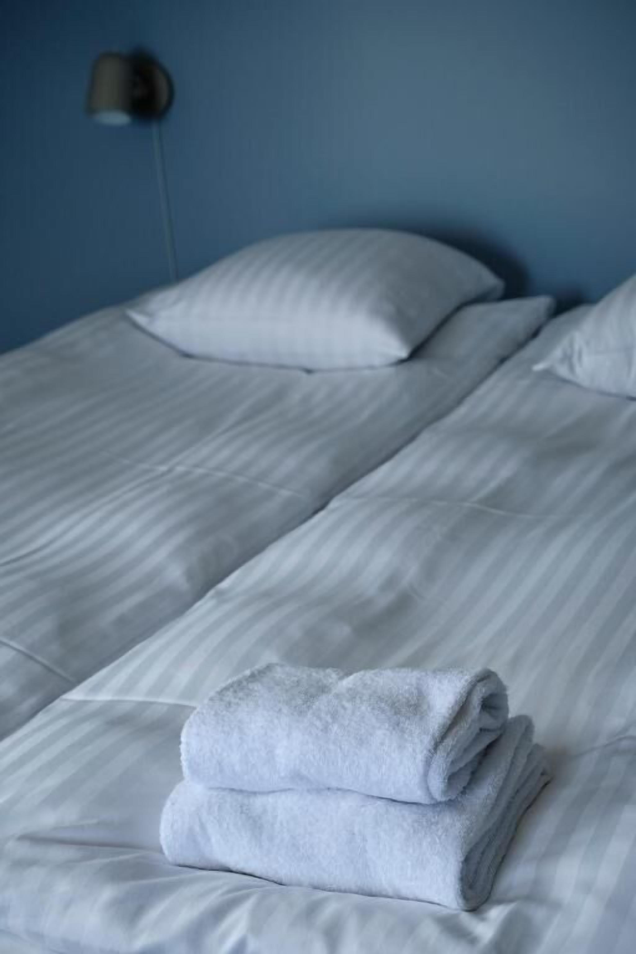 A hotel room with two beds, white bedding, and a folded towel on the bed.