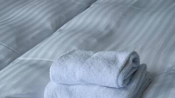 Een hotelkamer met twee bedden, wit beddengoed en een opgevouwen handdoek op het bed.