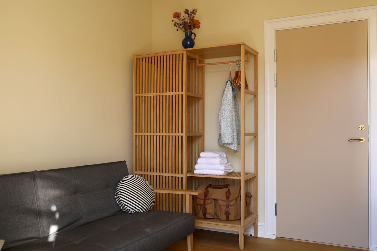 A room with a grey sofa, a wooden wardrobe, a vase with dried flowers, and a closed door.