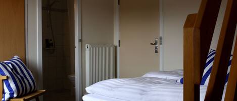 Una camera d'albergo con un letto, una doccia e una sedia di legno.