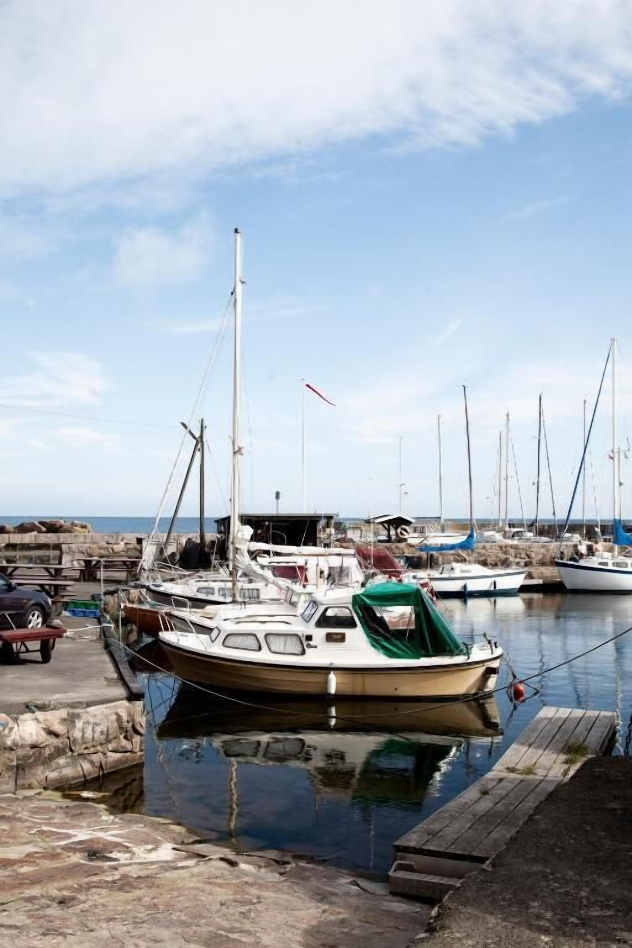 En lysthavn med flere både fortøjet, en træbrygge og et roligt hav i baggrunden.
