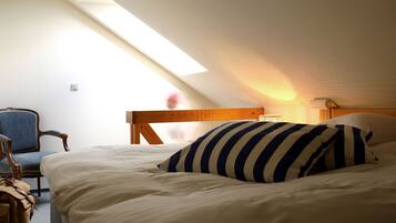 A bedroom with a sloped ceiling, a bed with white bedding and striped pillows, a wooden headboard, a chair, and a lamp.