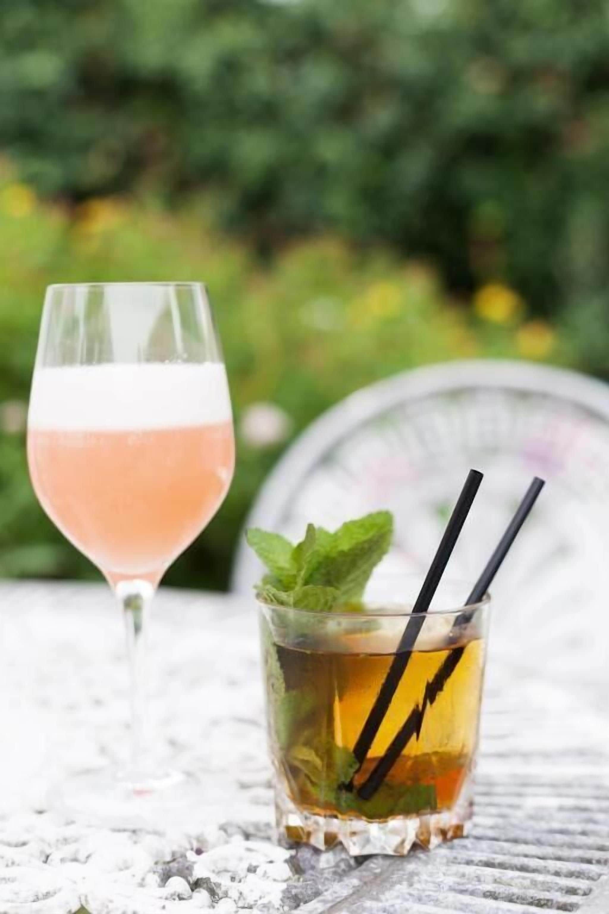 Two glasses of beverages on a metal table with a blurred green background.