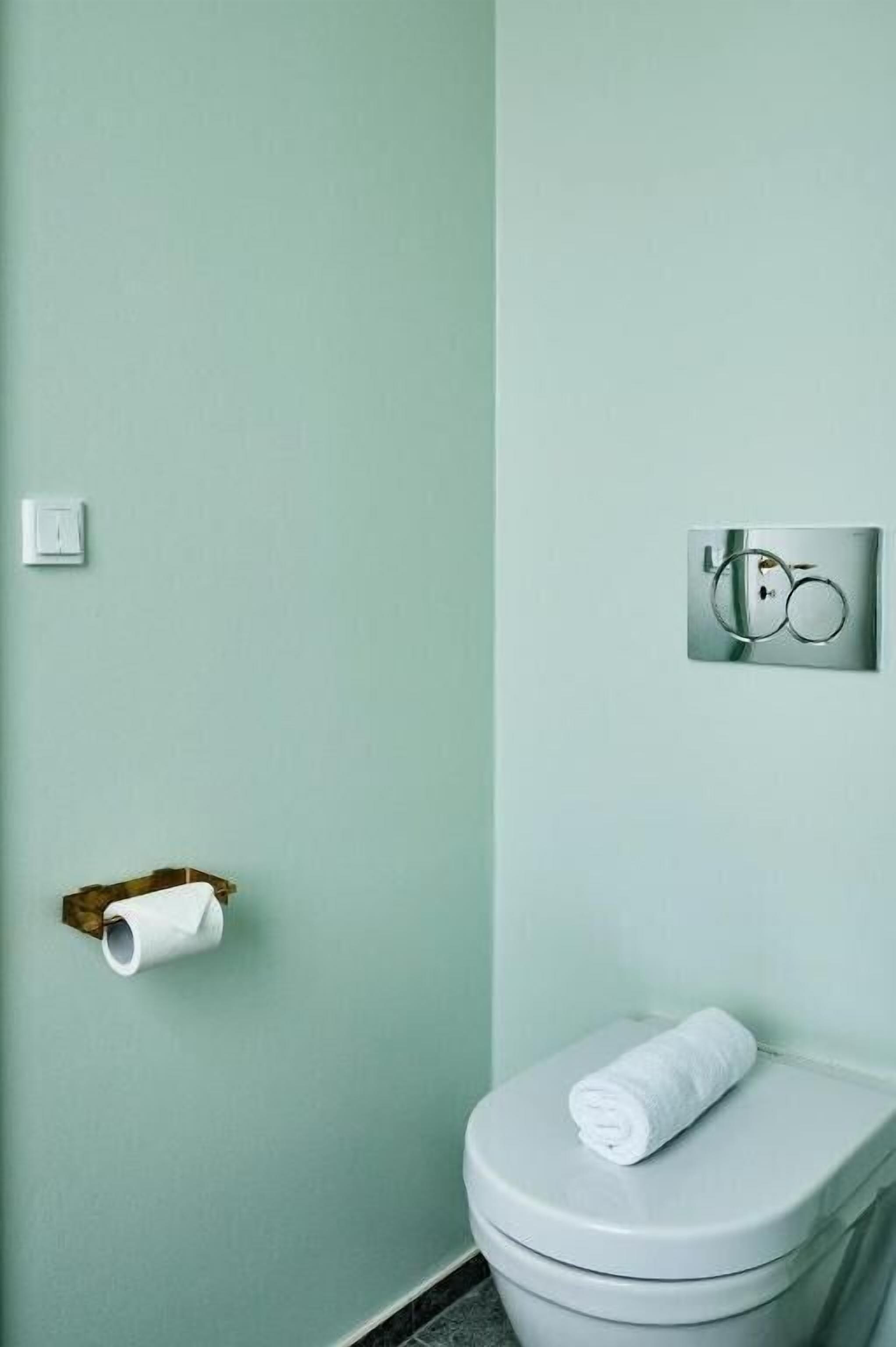 A bathroom with a toilet, a toilet paper holder, and a towel on the toilet seat.