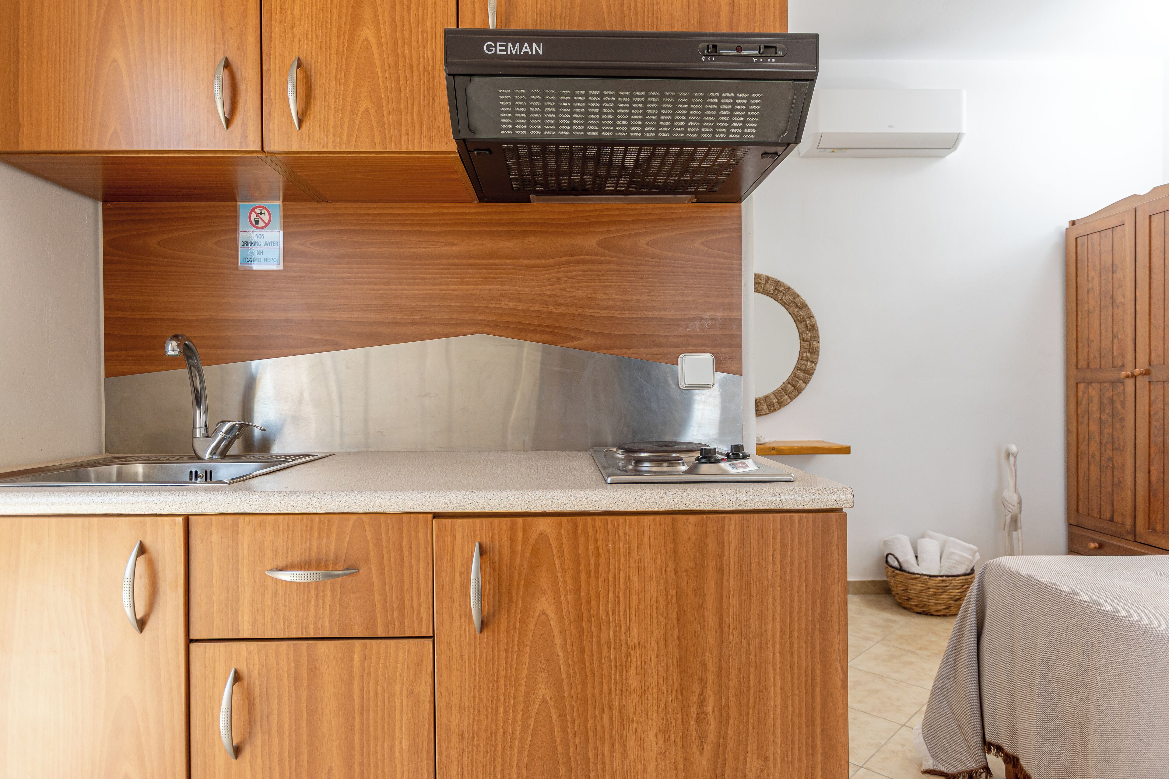 A compact kitchen with wooden cabinets, a stainless steel sink, a built-in oven, and a wall-mounted air conditioner.