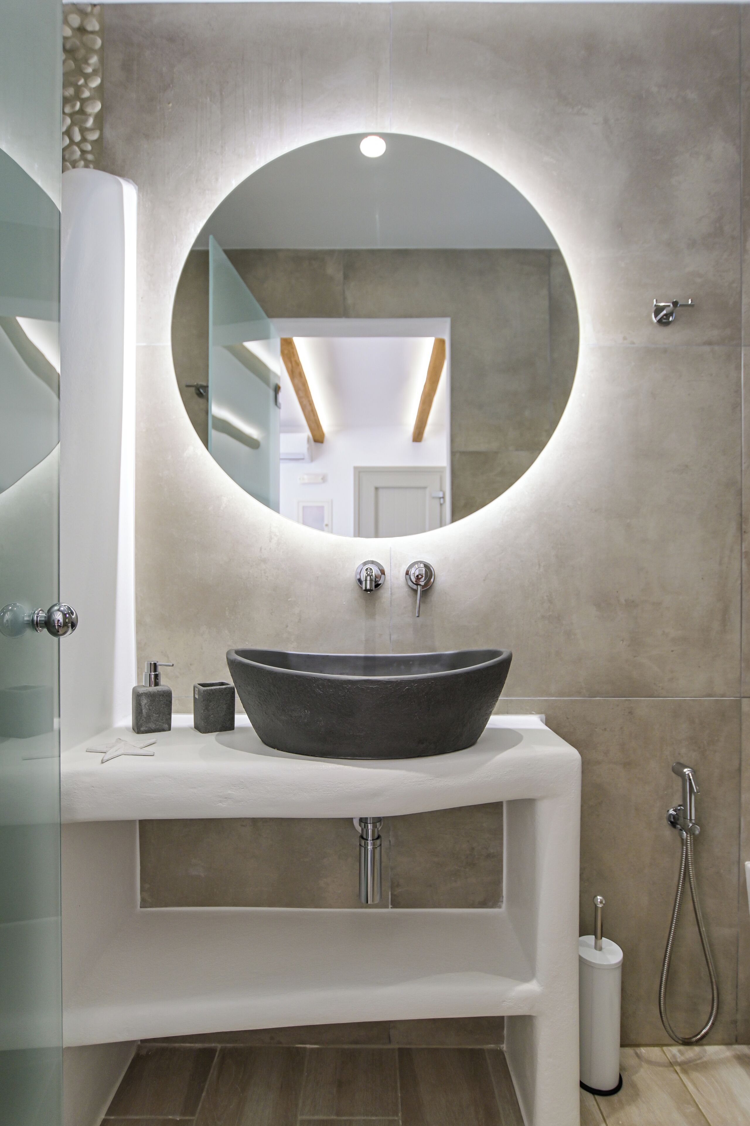A modern bathroom with a large round mirror, a vessel sink, and a shower.