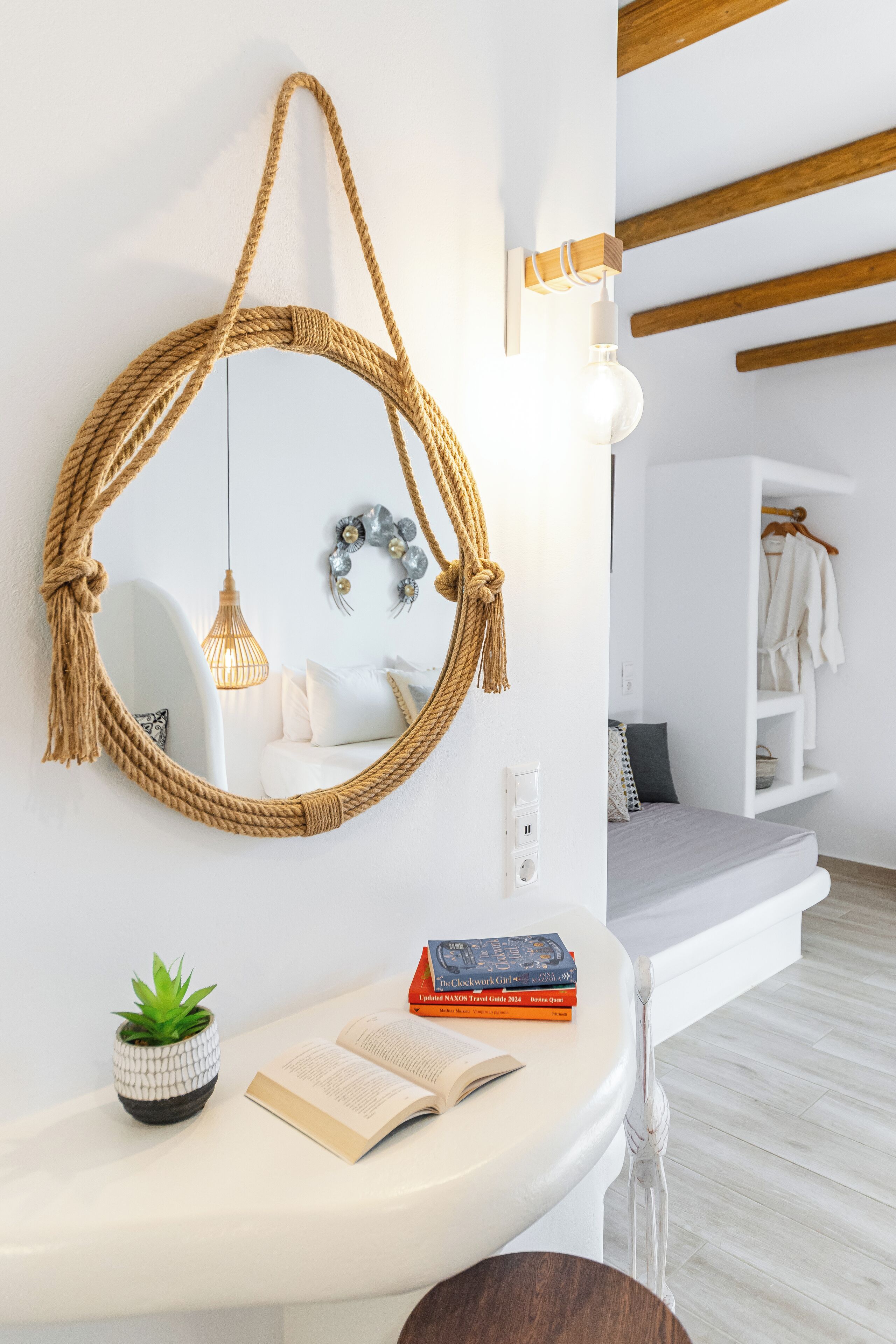A modern bathroom with a round mirror, a hanging light fixture, a small potted plant, and a book on the vanity.