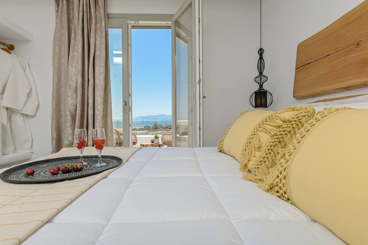 A bedroom with a bed, a tray with strawberries and drinks, a view of the outdoors, and a wooden headboard.