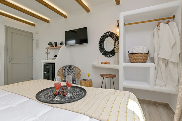 Un dormitorio moderno con cama, mesita de noche, televisor y estante en la pared con toallas y una cesta.