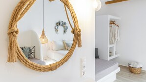 Une pièce avec un grand miroir rond, un luminaire suspendu, un canapé blanc et une étagère en bois où sont posés des vêtements.