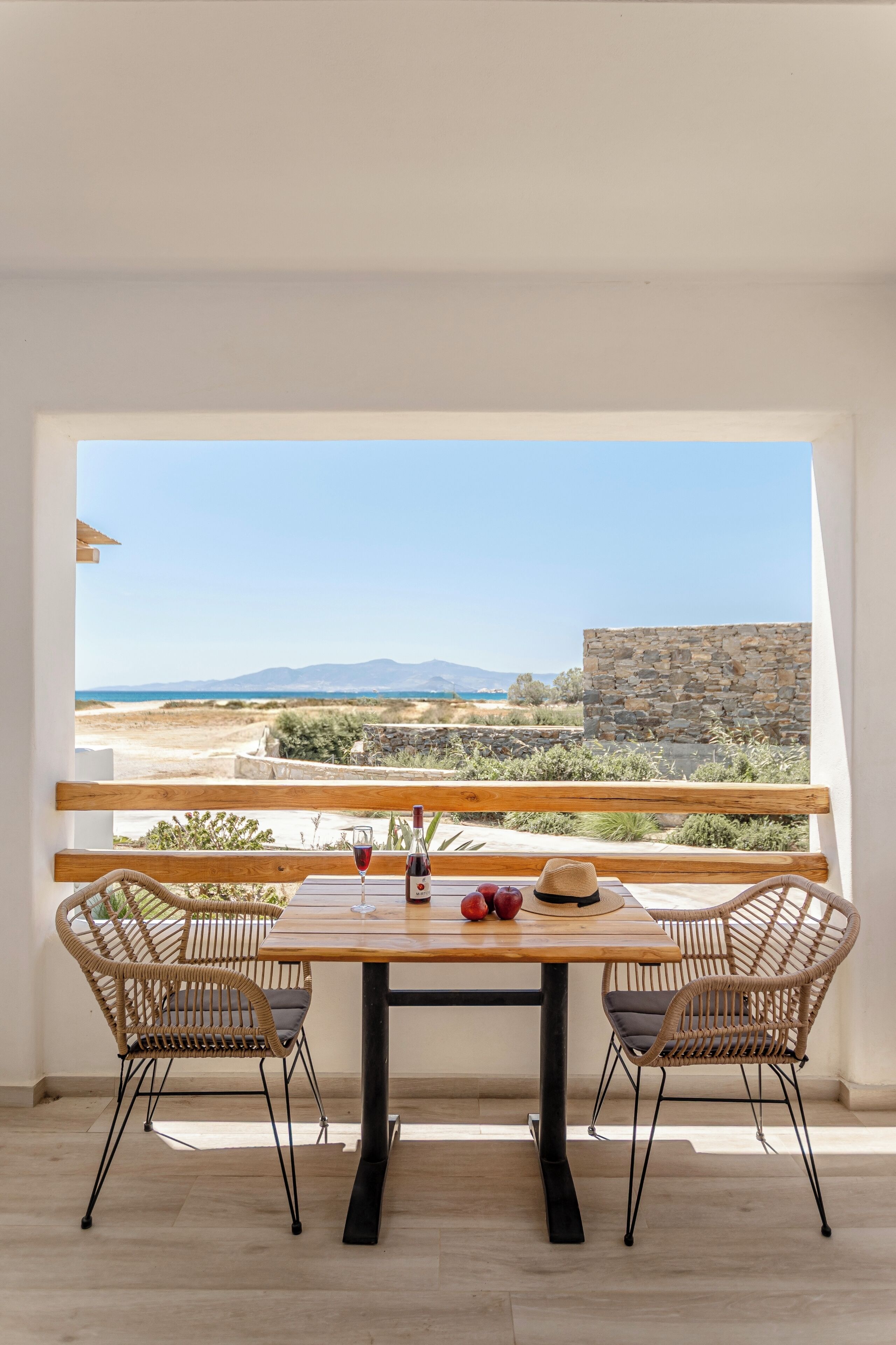 Ein Balkon mit Tisch und Stühlen, Blick auf den Strand und eine Steinmauer.