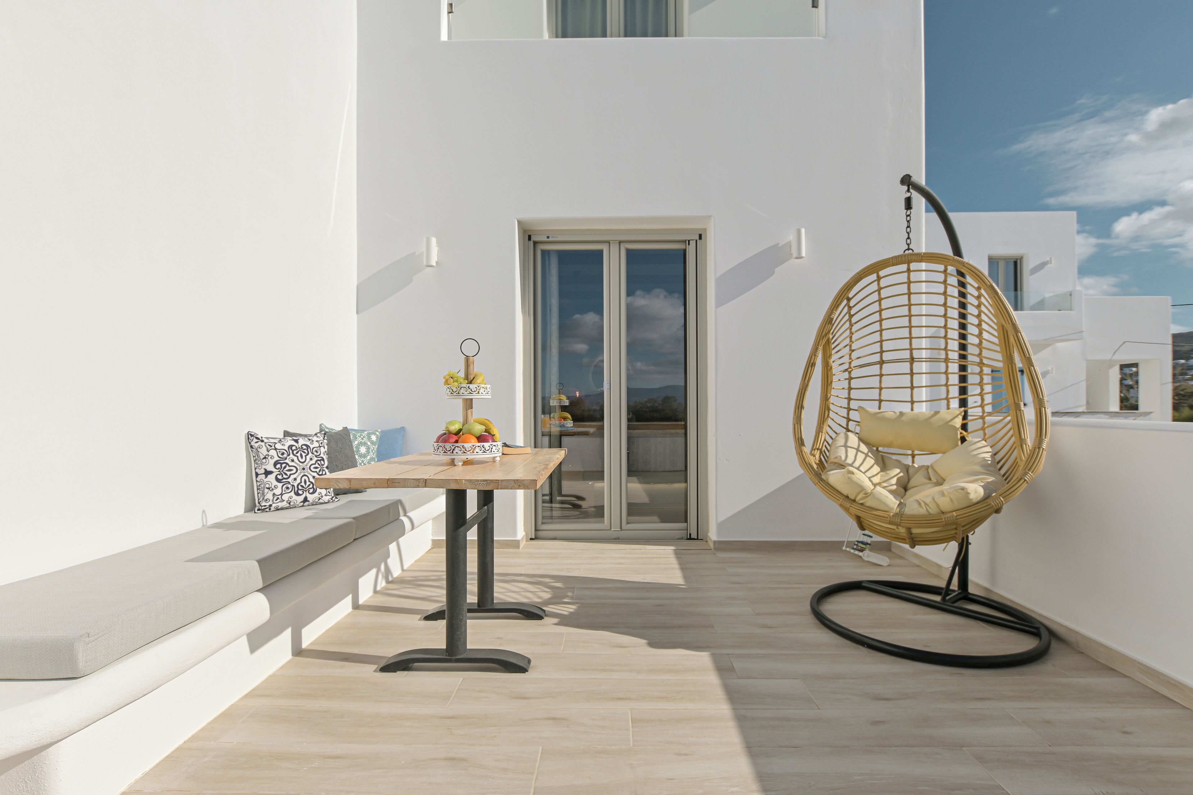 A balcony with a table, a wicker chair, and a bench.