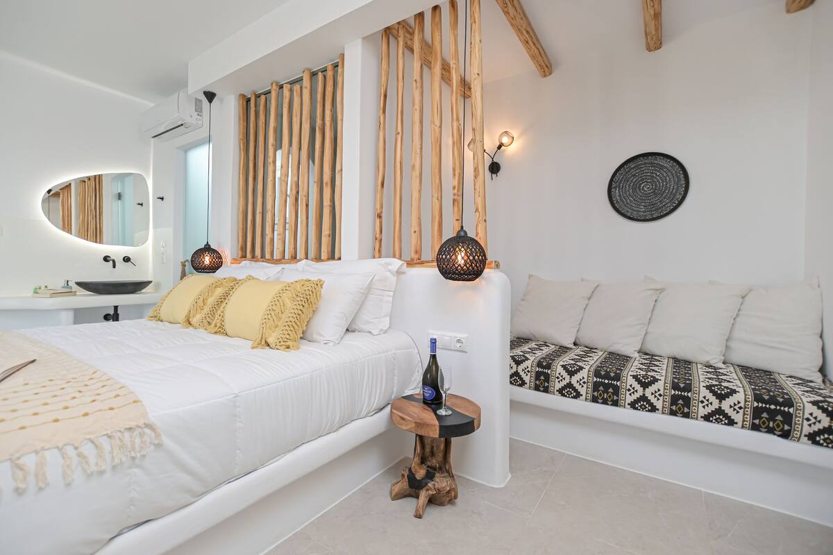 A modern bedroom with a white bed, a wooden headboard, and a patterned sofa.