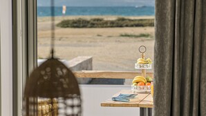 Une vue sur une plage, prise à travers une fenêtre, avec une table sur laquelle sont disposés des fruits et un magazine.
