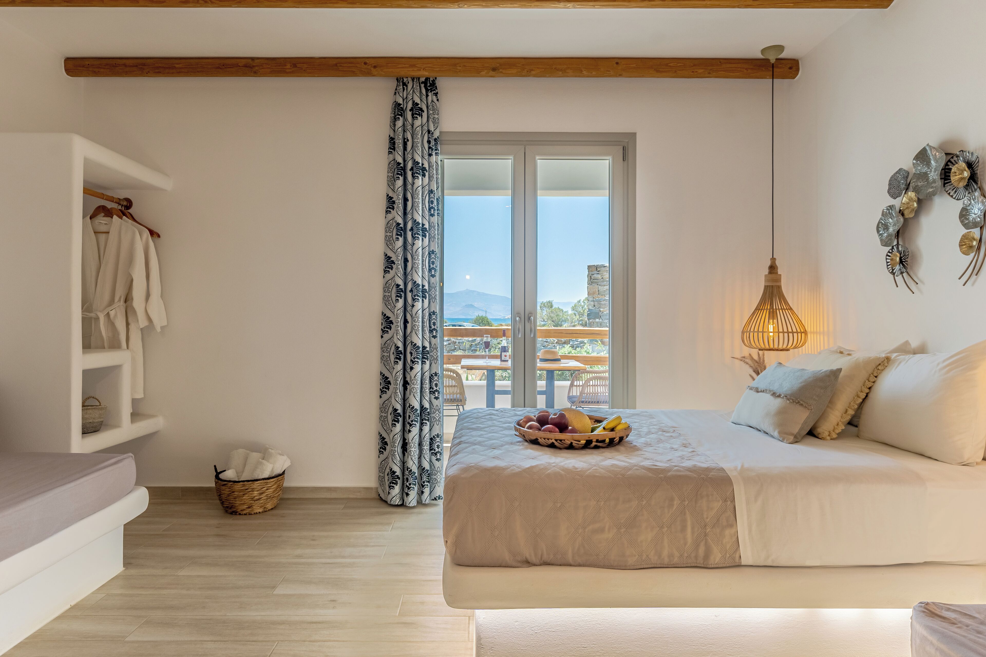 A bedroom with a bed, a bedside table, a hanging light fixture, a window with a view, and a basket on the floor.