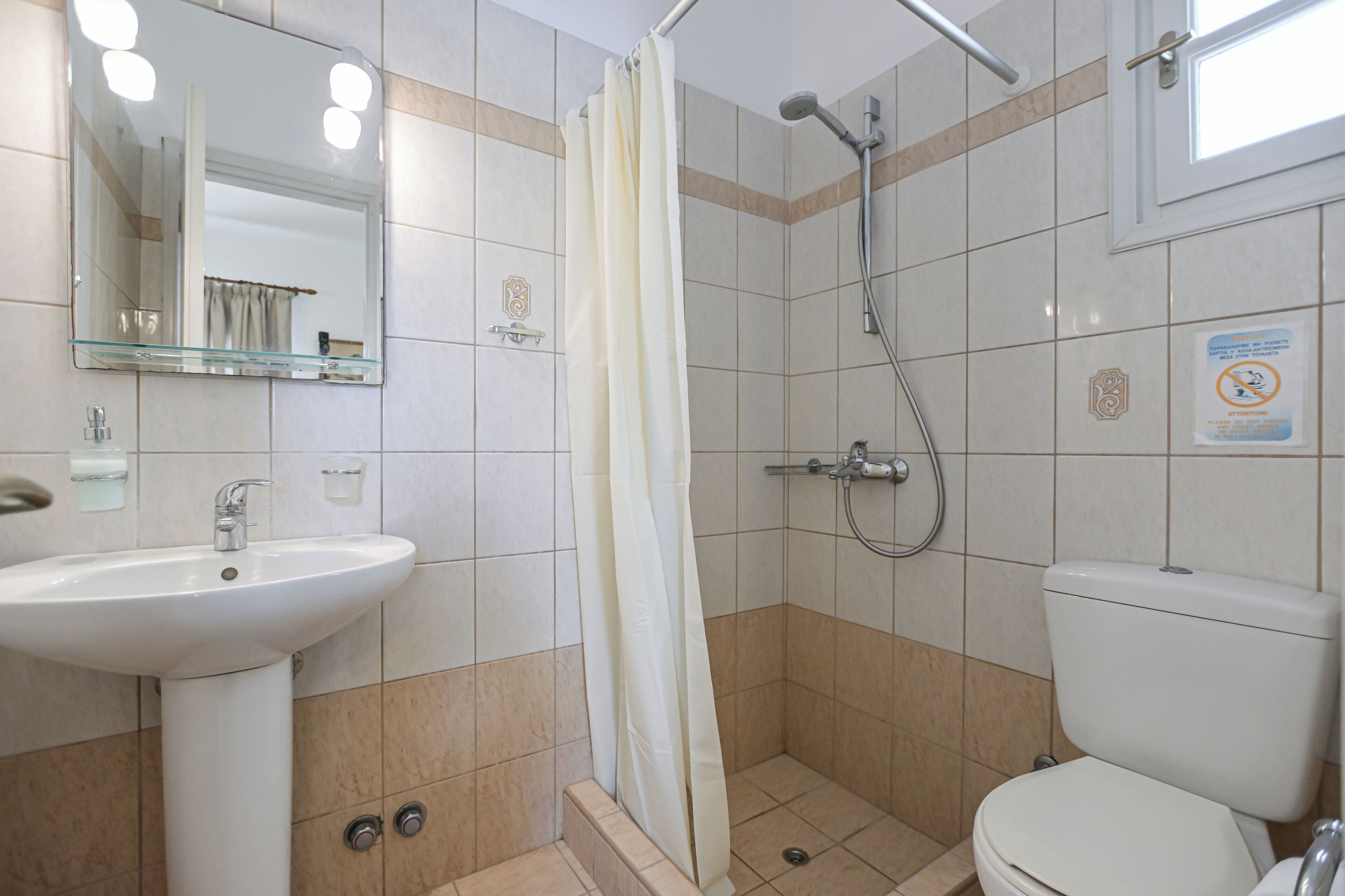 A bathroom with a sink, toilet, shower, and a mirror with lights.