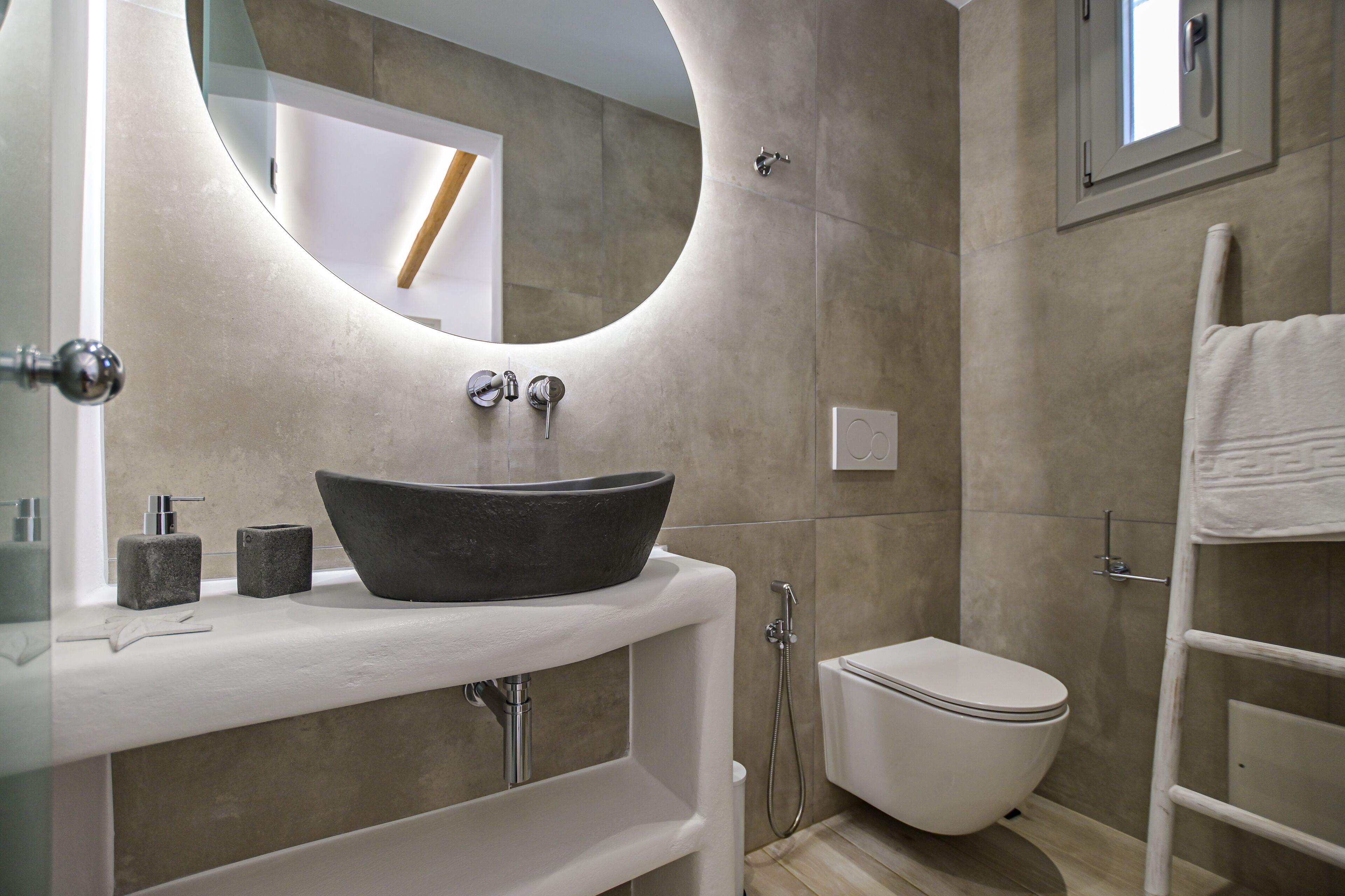A modern bathroom with a round mirror, a black vessel sink, a toilet, and a shower.