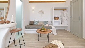 Une salle de bain moderne avec un banc en bois, une table ronde en bois sur laquelle est posé un panier de fruits, un porte-serviettes et un luminaire fixé au mur.