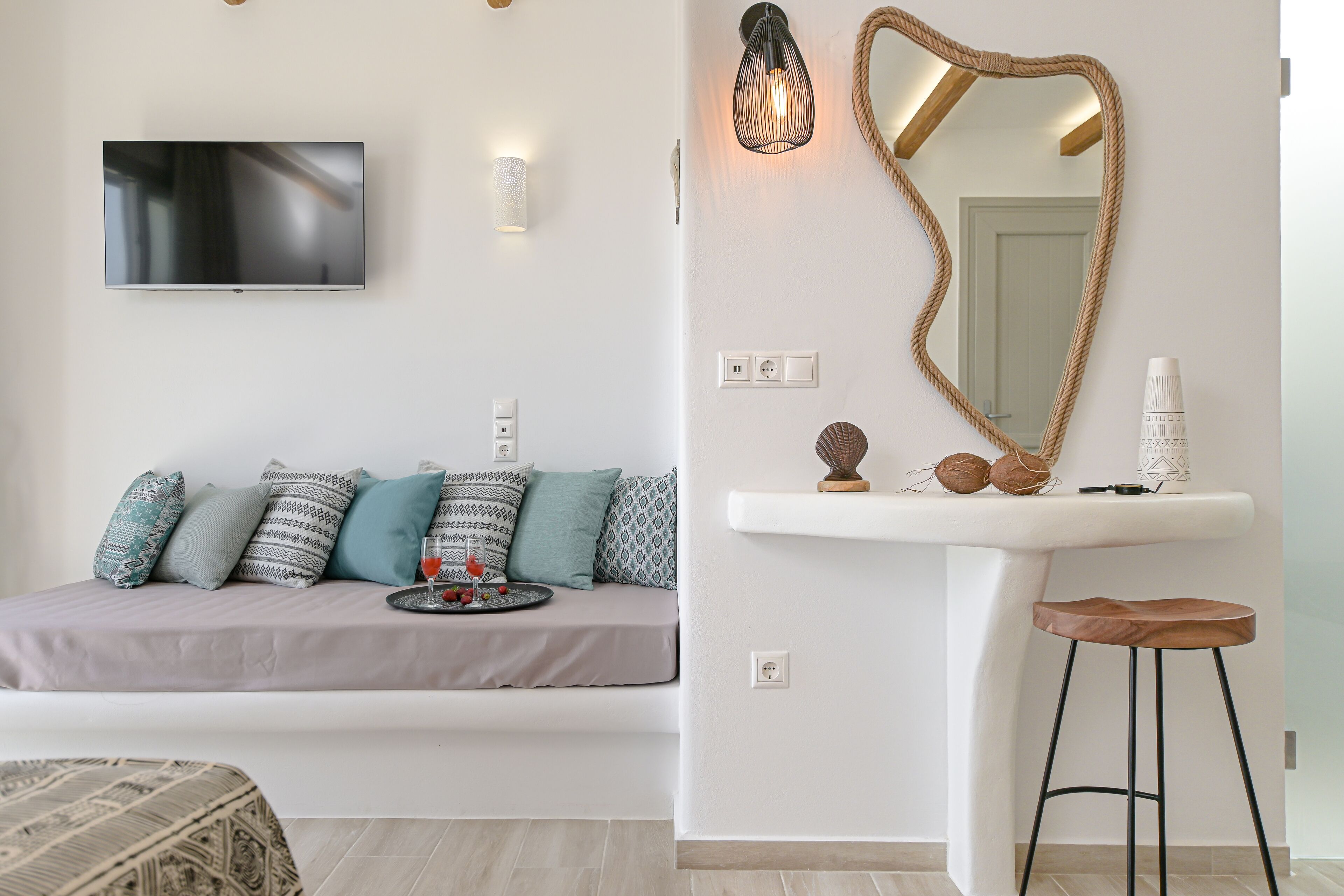 A modern living room with a sofa, a TV, a wall-mounted mirror, and a white pedestal table with a stool.