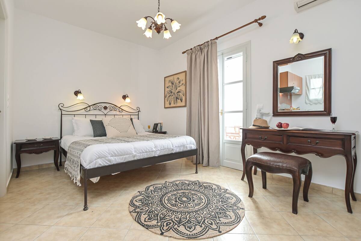 A bedroom with a bed, bedside tables, a dresser, a mirror, a chandelier, and a window with curtains.