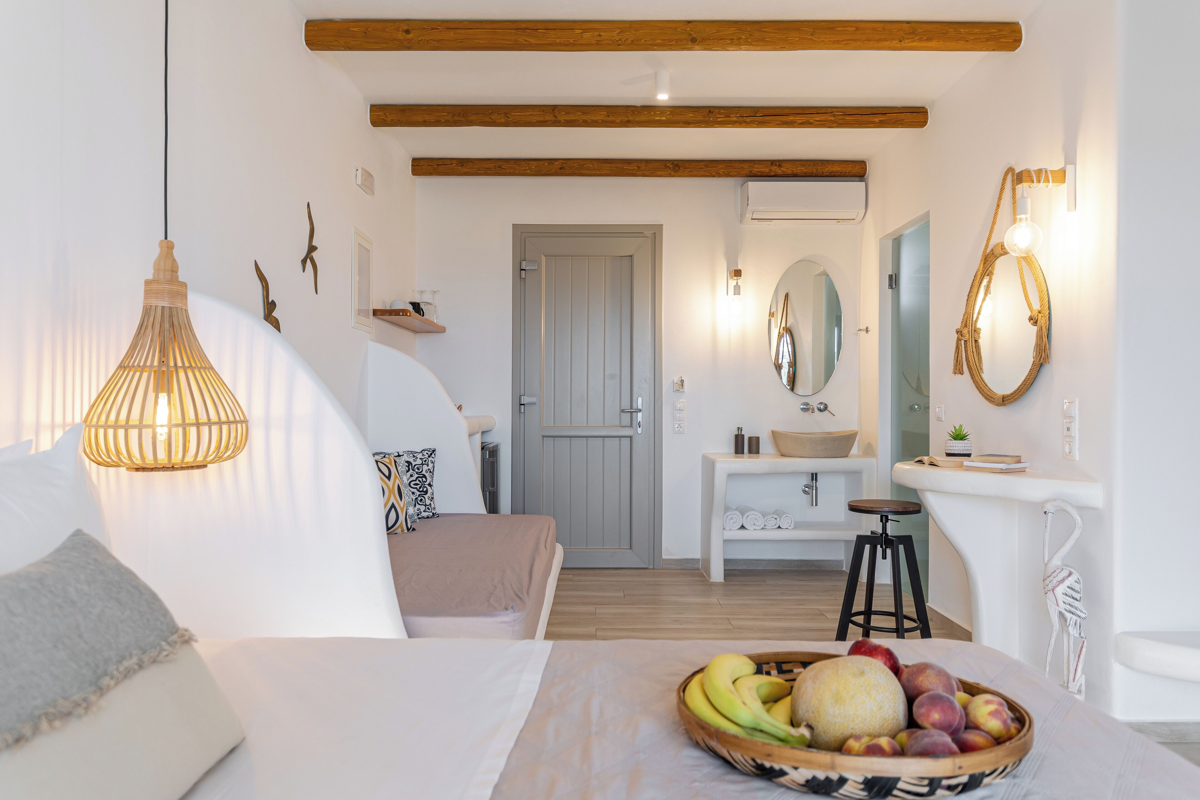 Un dormitorio moderno con cama, mesita de noche y frutero. Cuenta con un baño con lavamanos y espejo.