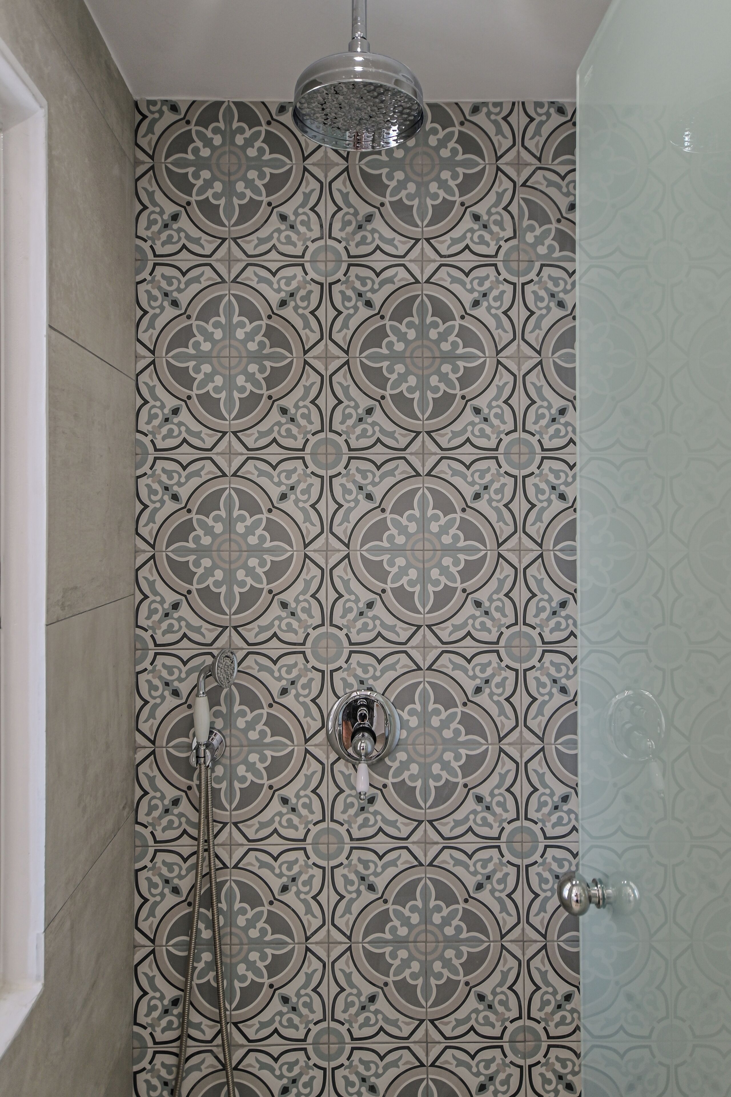 A shower with a patterned tile wall, a glass shower door, and a handheld showerhead.