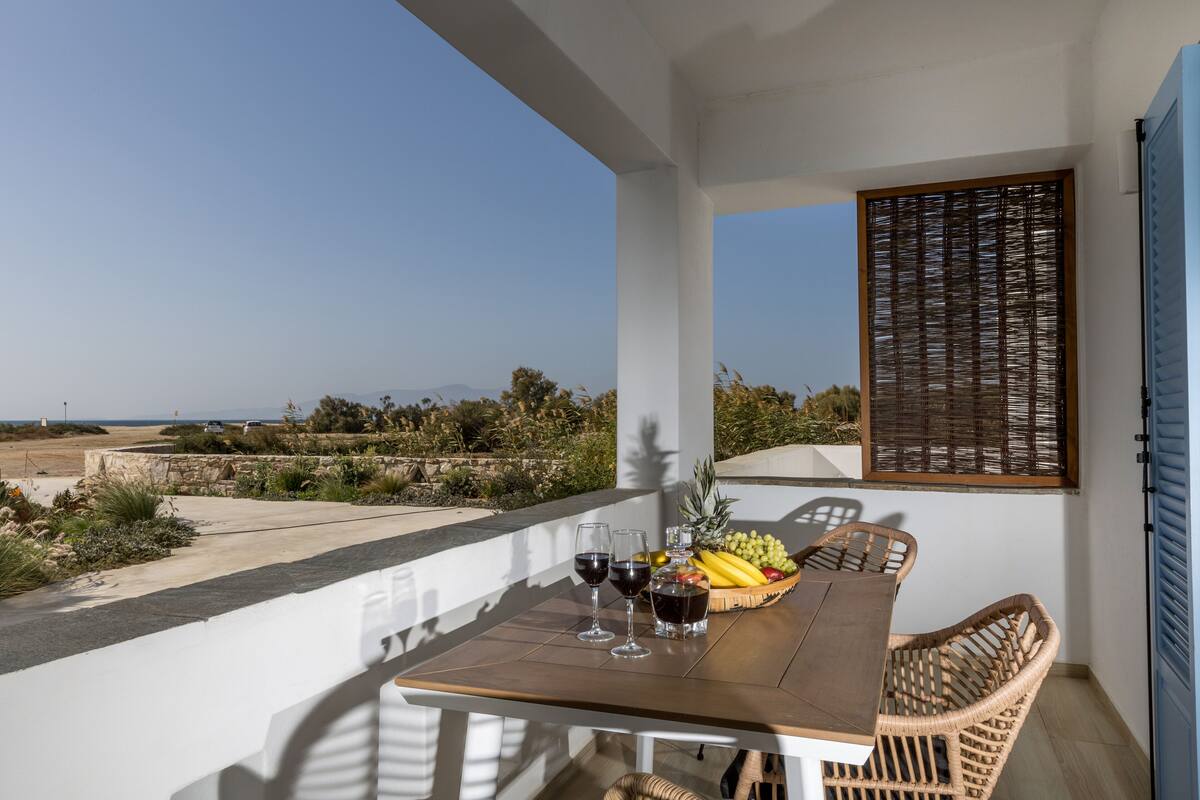 A balcony with a table set for two, featuring a bottle of wine, glasses, and a fruit basket.