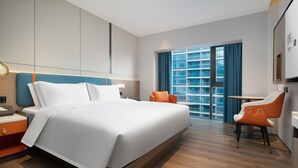 Ett modernt hotellrum med en stor säng, ett skrivbord och en stol. Det finns ett fönster med gardiner och utsikt över en byggnad.