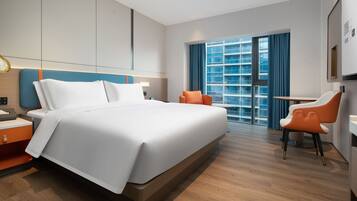 Een moderne hotelkamer met een groot bed, een bureau en een stoel. Er is een raam met gordijnen en uitzicht op een gebouw.