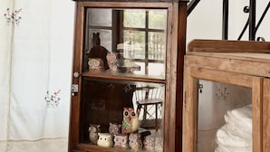 A wooden cabinet with an owl figurine on top, glass doors, and a lace curtain with floral patterns. - Sleep Owl Chiang Mai  (Chiang Mai)