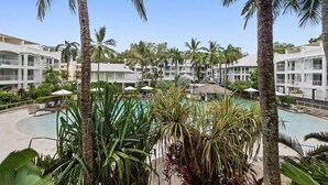 A resort with multiple white buildings, palm trees, and a central swimming pool surrounded by lounge areas.