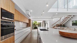 A modern kitchen with built-in appliances, a central island, and a staircase leading to an upper level. - Beachmont Bliss Palm Cove 3 Bedroom Holiday Home (Palm Cove)
