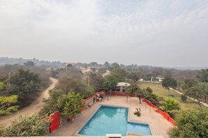A rectangular pool with a red fence, surrounded by greenery and a view of distant buildings.