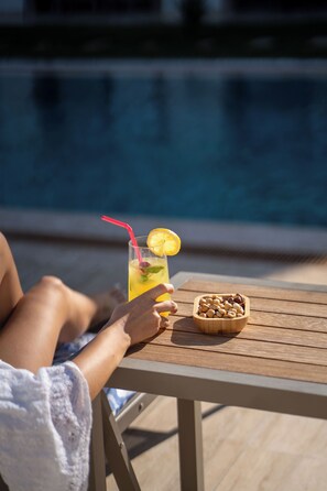 A person relaxing by a poolside table with a drink and nuts. - Hane Cunda (Ayvalik)