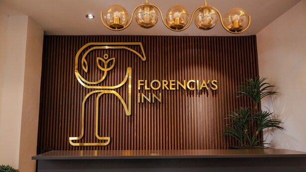 Un comptoir d’accueil avec un panneau en bois en arrière-plan, un grand logo doré et une enseigne indiquant « Florencia’s Inn ».