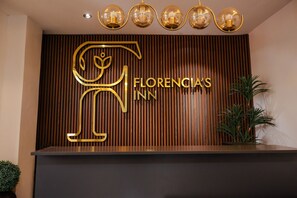 A reception desk with a wooden panel background, a large golden logo, and a sign reading "Florencia's Inn".