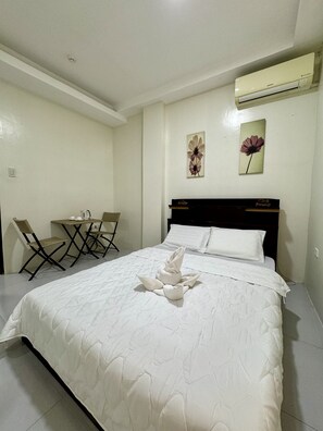 A hotel room with a neatly made bed, a small table with chairs, and an air conditioning unit on the wall.