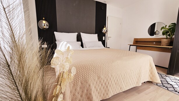 A bedroom with a large bed, a bedside table, a mirror, and a potted plant. - Apartment Marina (Oberzent)