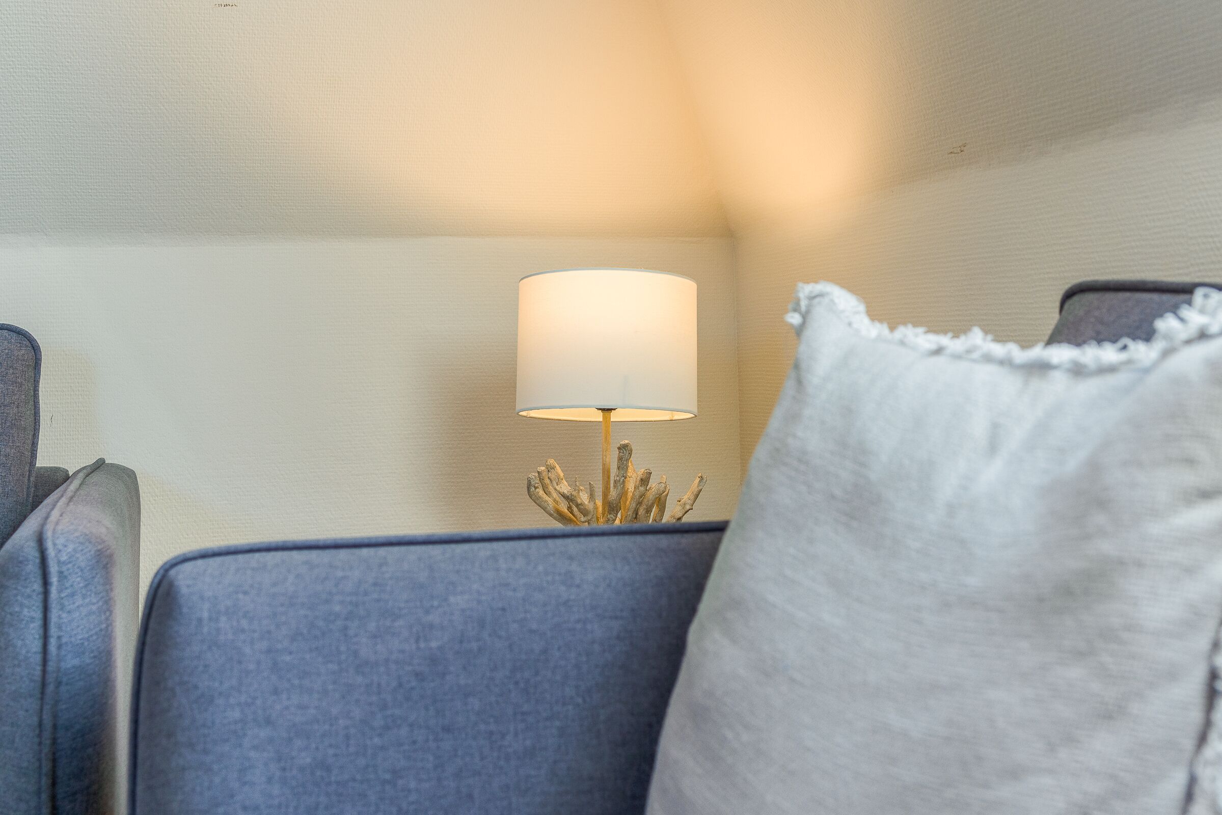 Una habitación con un cabecero tapizado en azul, un cojín blanco y una lámpara con pantalla blanca.
