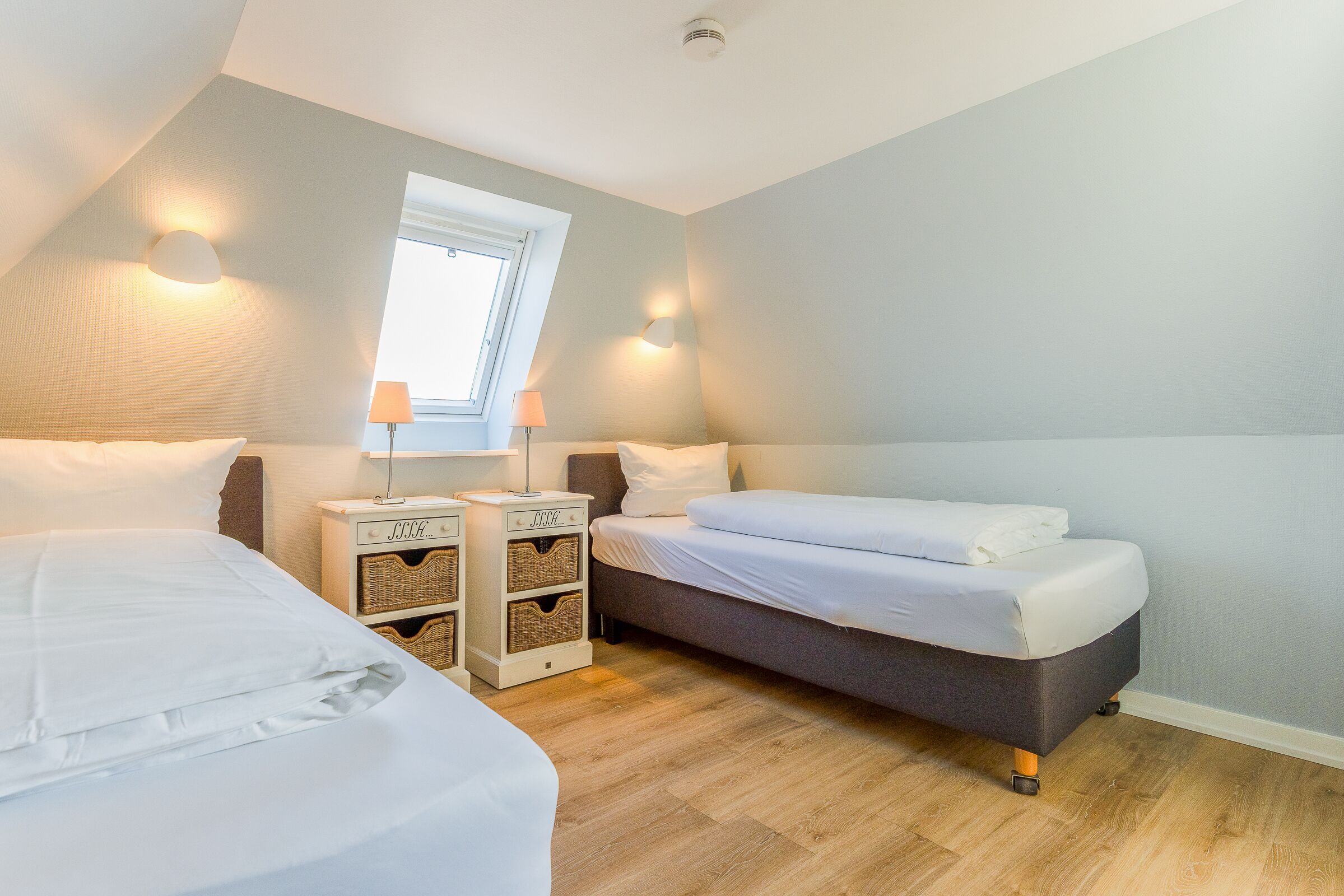 A bedroom with two beds, a window, and a nightstand with baskets.