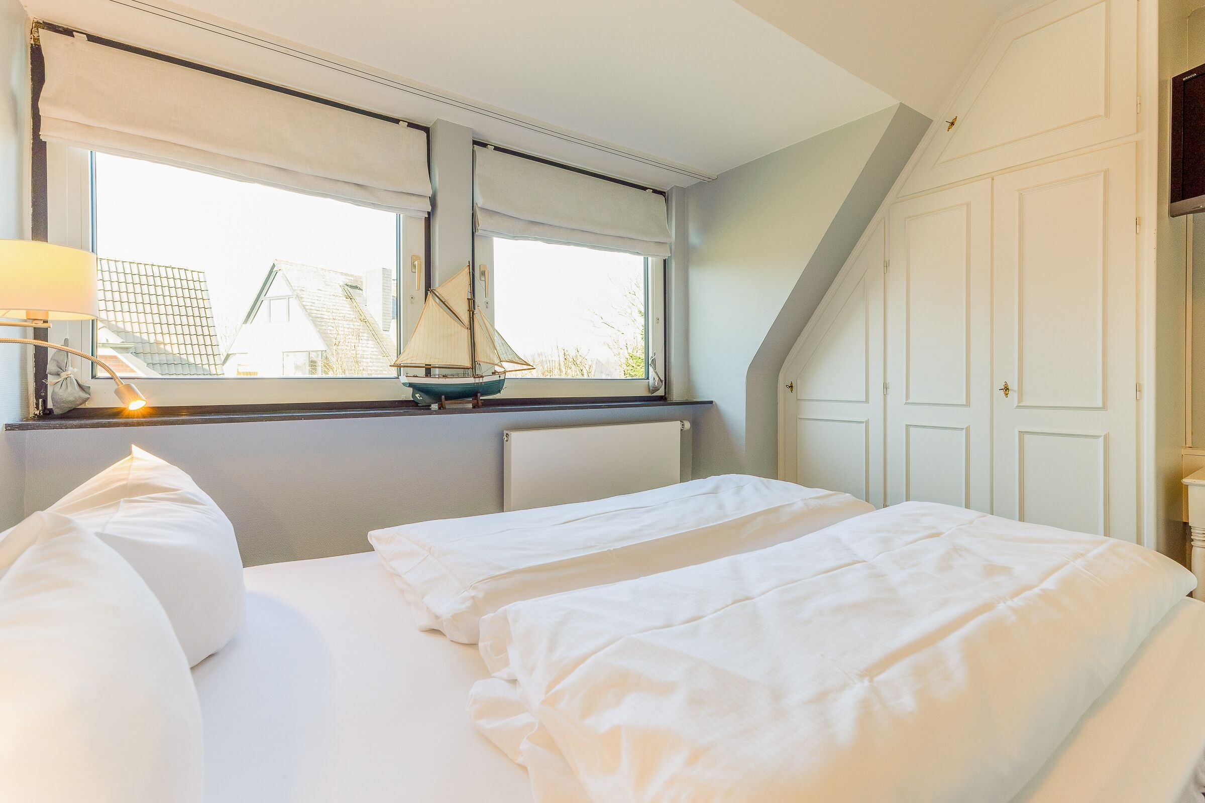 Un dormitorio con dos camas, una ventana que ofrece vistas a edificios y una lámpara en la mesita de noche.