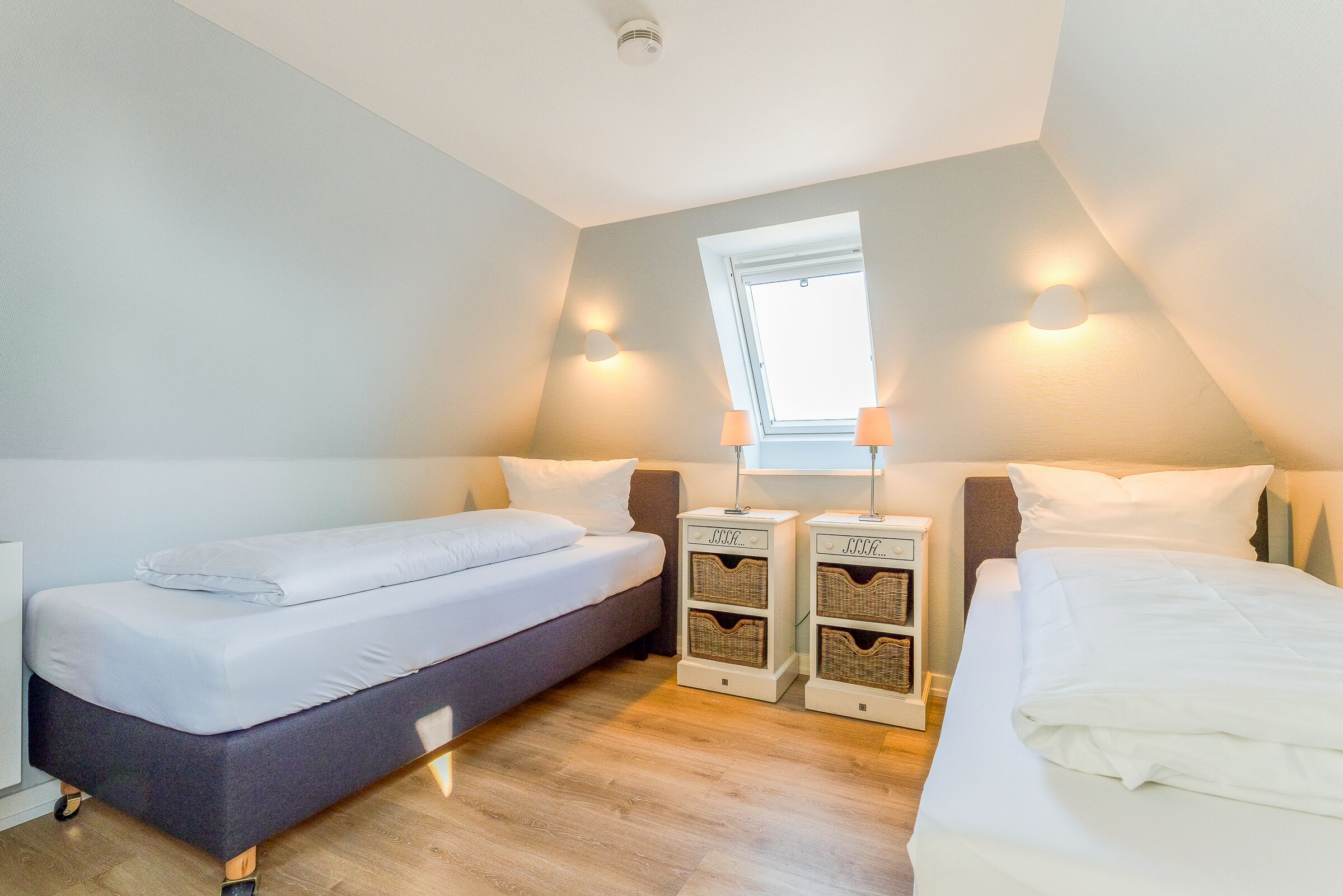 A bedroom with two beds, a window, and two nightstands with baskets.